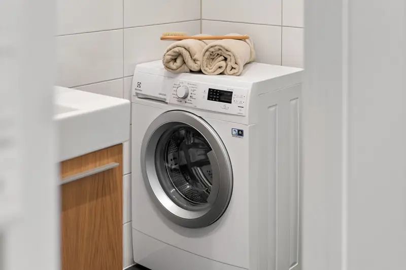 A washing machine with rolled towels on top in a white utility room