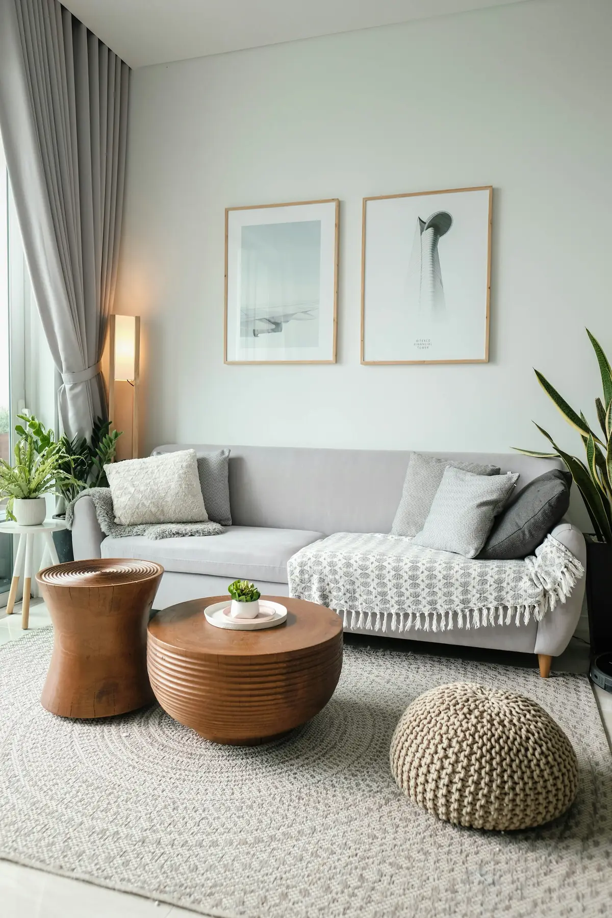 A light living room with a grey sofa, wooden side tables and plants.