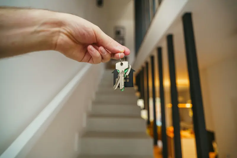 A hand holding house keys at the foot of a staircase