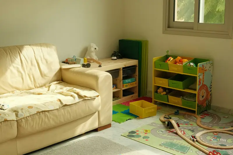 A playroom with a sofa, toy storage and a wooden train track on the play mat